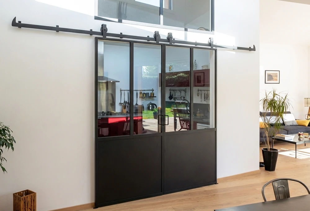 Intérieur moderne avec cloison verrière coulissante type atelier, séparant un salon d'une cuisine ouverte