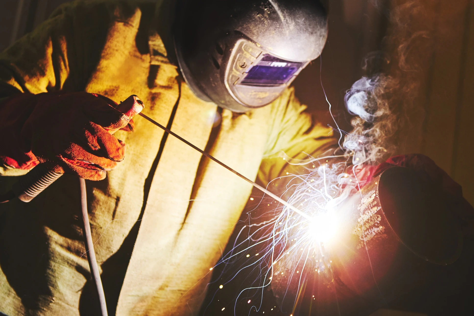 Soudeur professionnel en action dans un atelier industriel, portant un masque de soudage à cristaux liquides et des gants de protection renforcés