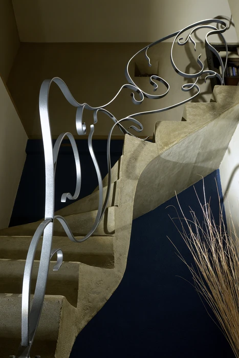 Escalier en pierre calcaire avec rampe en fer forgé argenté aux volutes artisanales fluides et organiques