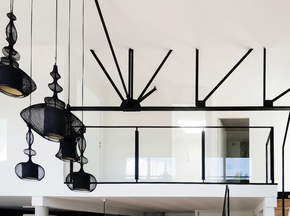 Intérieur contemporain double hauteur, garde-corps vitré à cadre métal noir, structure porteuse en fermes métalliques noires rayonnantes