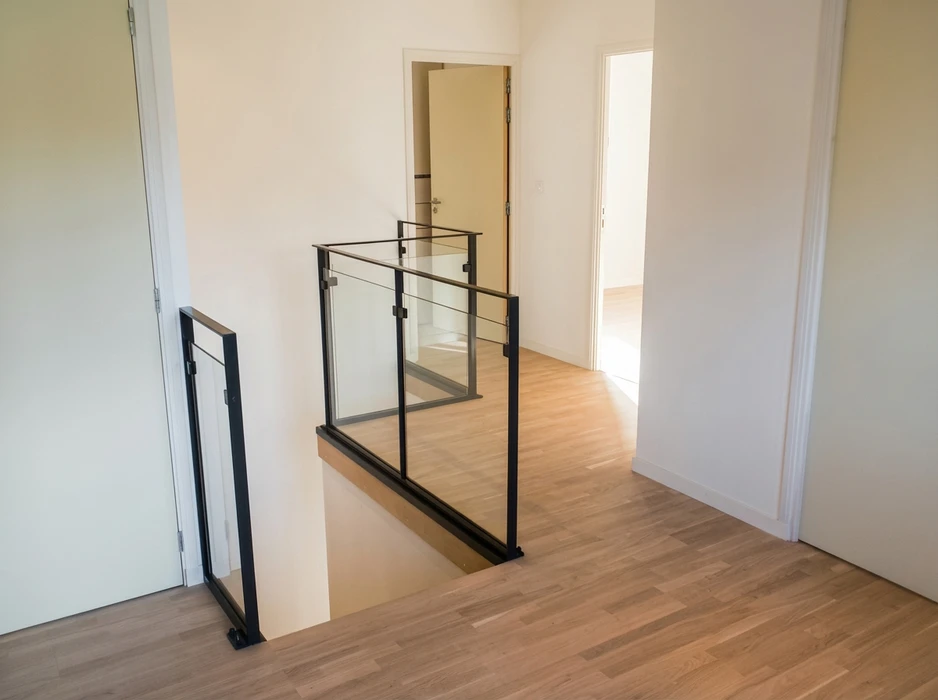 Palier d'étage avec garde-corps en acier noir mat et panneaux en verre trempé, vue depuis le haut d'un escalier