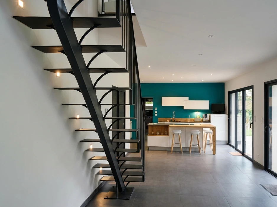 Escalier métallique design noir à marches ouvertes avec crémaillère courbée, intégré dans un espace de vie ouvert