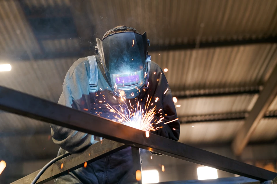 Ouvrier en combinaison bleue et casque jaune travaille sur une machine-outil dans un atelier industriel