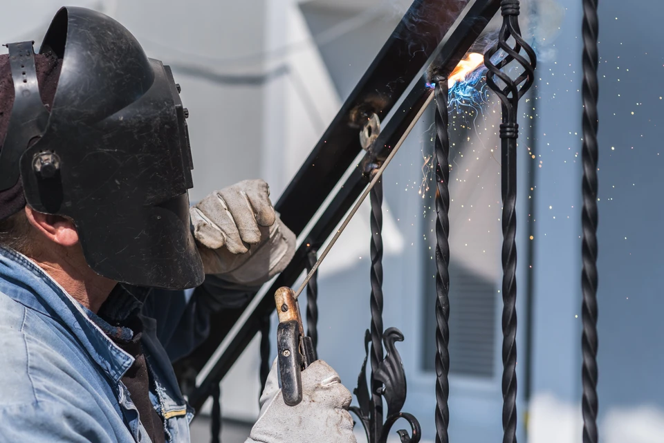 Soudeur professionnel travaillant dans un atelier industriel, portant un masque de protection et manipulant un chalumeau produisant des étincelles intenses sur une pièce métallique